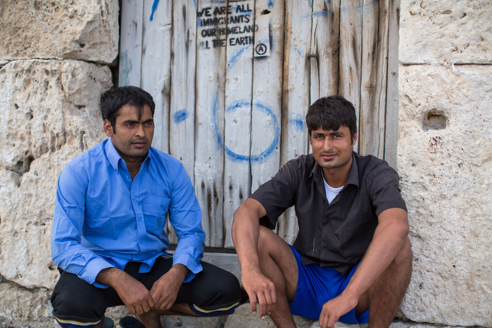 47303482 - kos, greece - sep 28, 2015: unidentified refugees. stencil on the wall: we are all immigrants, our homeland all the earth.